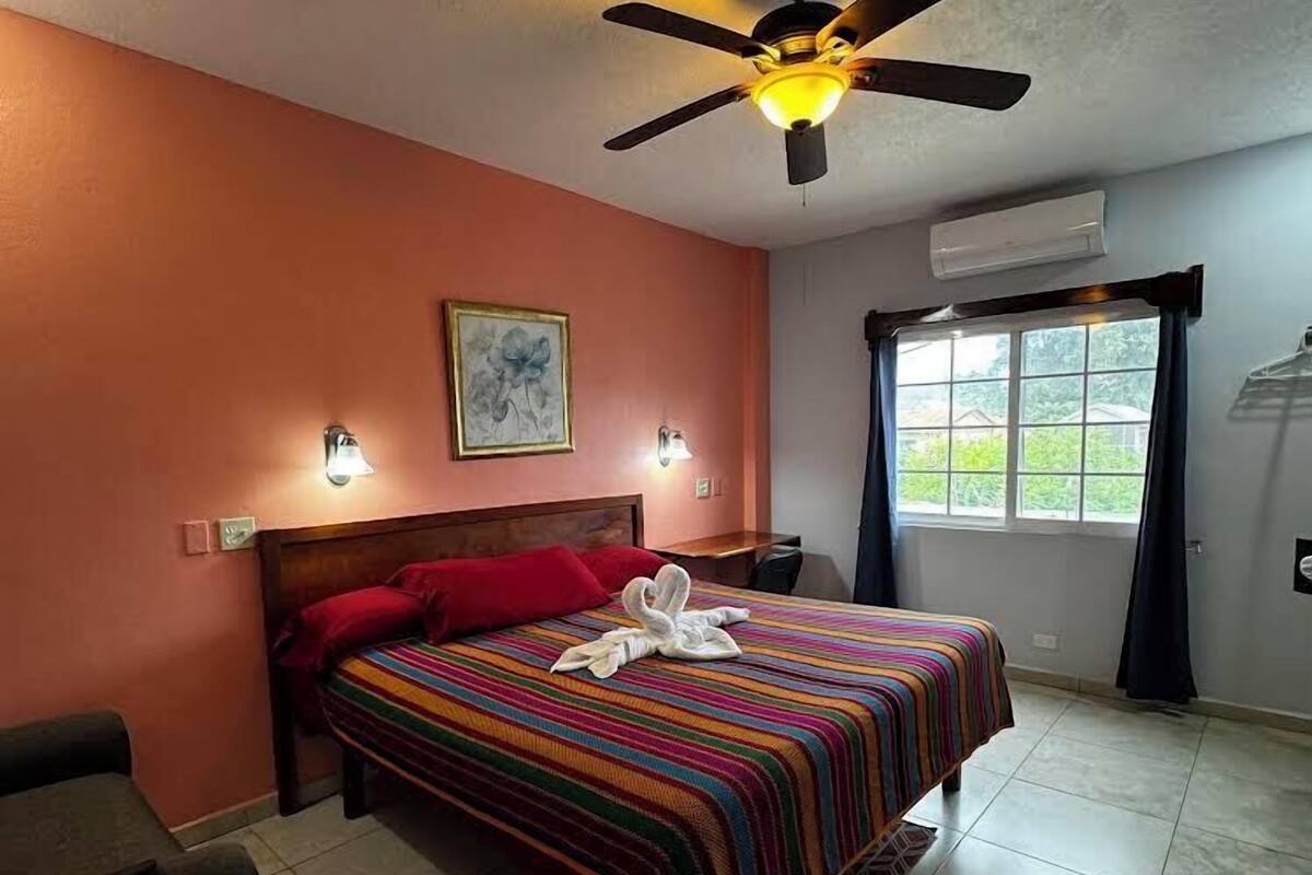 Quarto com cama, ventoinha no teto, janela com cortinas e ar condicionado.