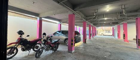 A parking garage with concrete floors and pink pillars, featuring a motorcycle and a car parked.