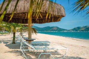 Une plage avec des parasols en chaume, des palmiers et des chaises longues en métal.