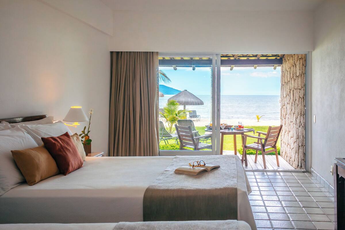 Een hotelkamer met een bed, een tafel en uitzicht op zee.