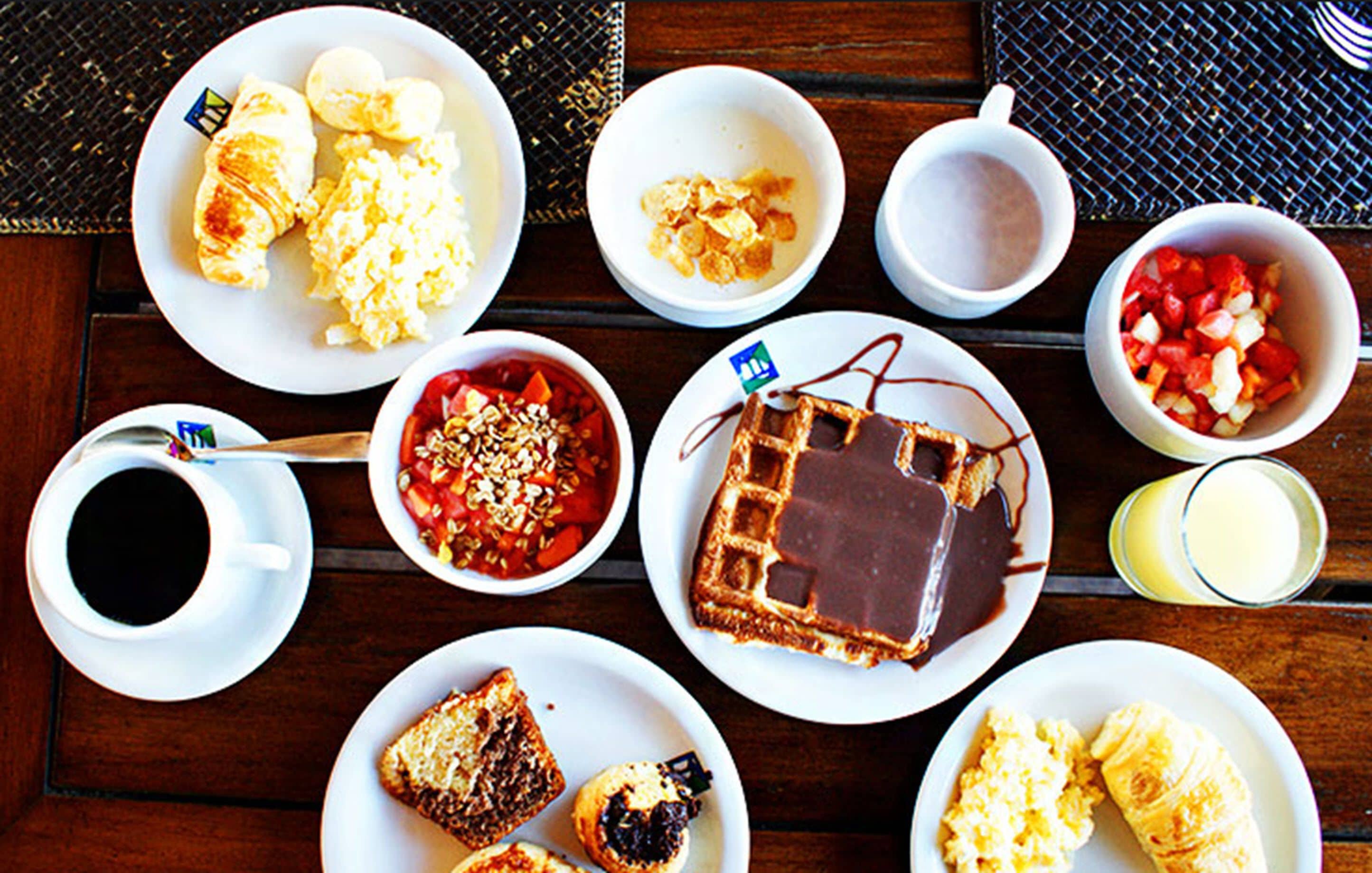 Une table de petit-déjeuner avec divers plats, notamment des croissants, des œufs brouillés, des gaufres et une tarte au chocolat.