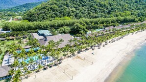 An aerial view of a beach resort with a swimming pool, beach umbrellas, and palm trees. - Portobello Resort & Safári (Mangaratiba)
