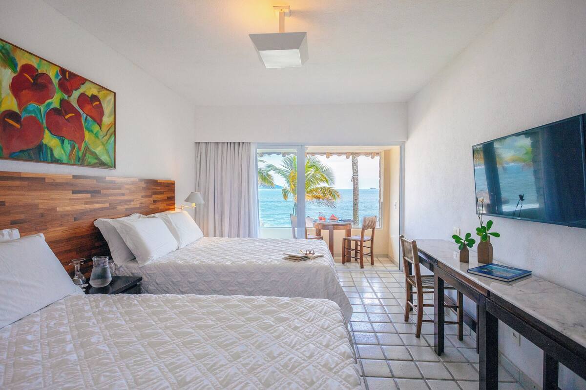 Een hotelkamer met twee bedden, een zithoek met tafel en stoelen, een televisie en uitzicht op de oceaan.