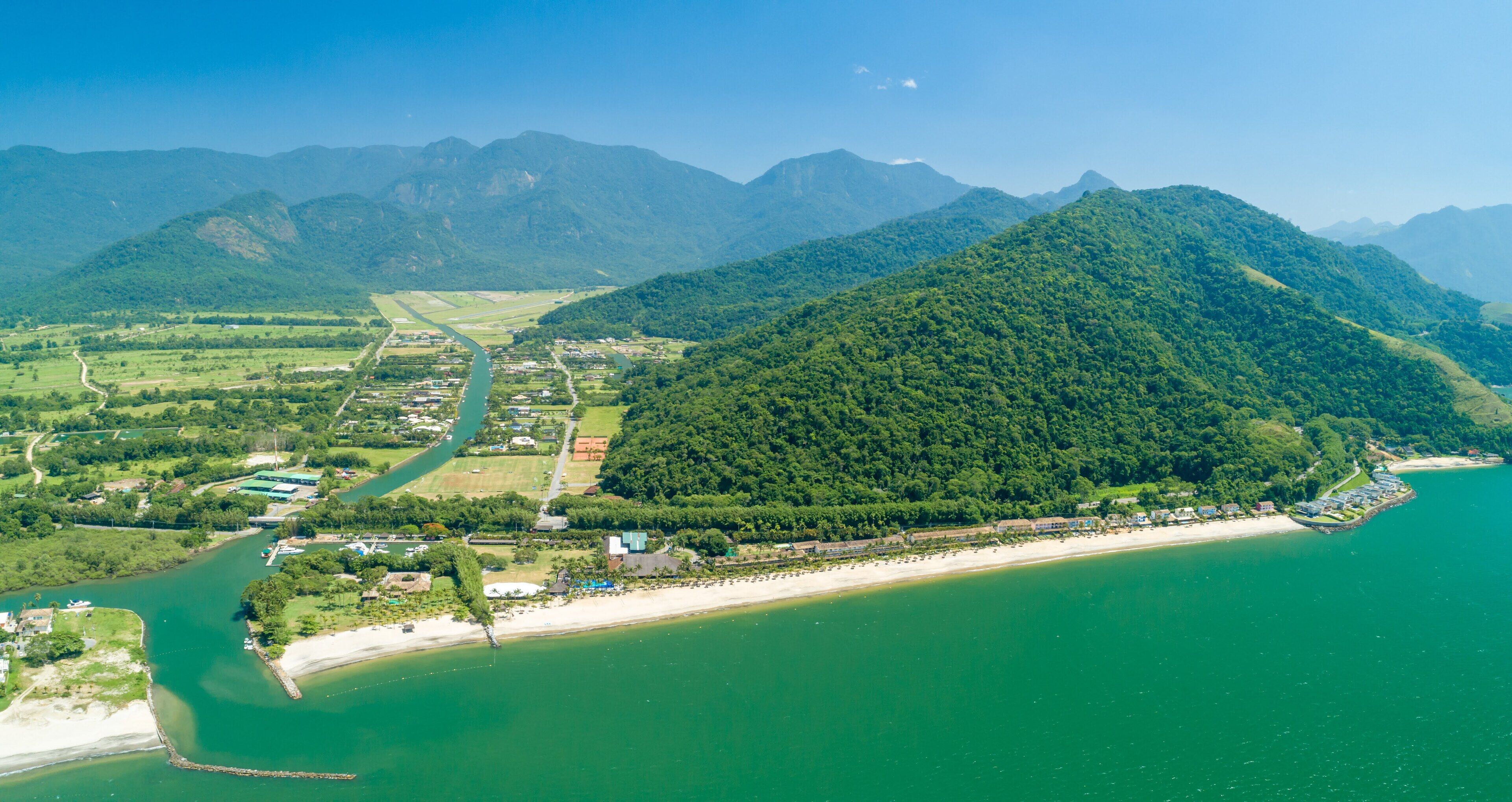 Vista aérea de una zona costera con playa, un río y montañas al fondo.