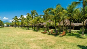 A resort with thatched-roof huts, palm trees, and sun loungers on a grassy lawn. - Portobello Resort & Safári (Mangaratiba)