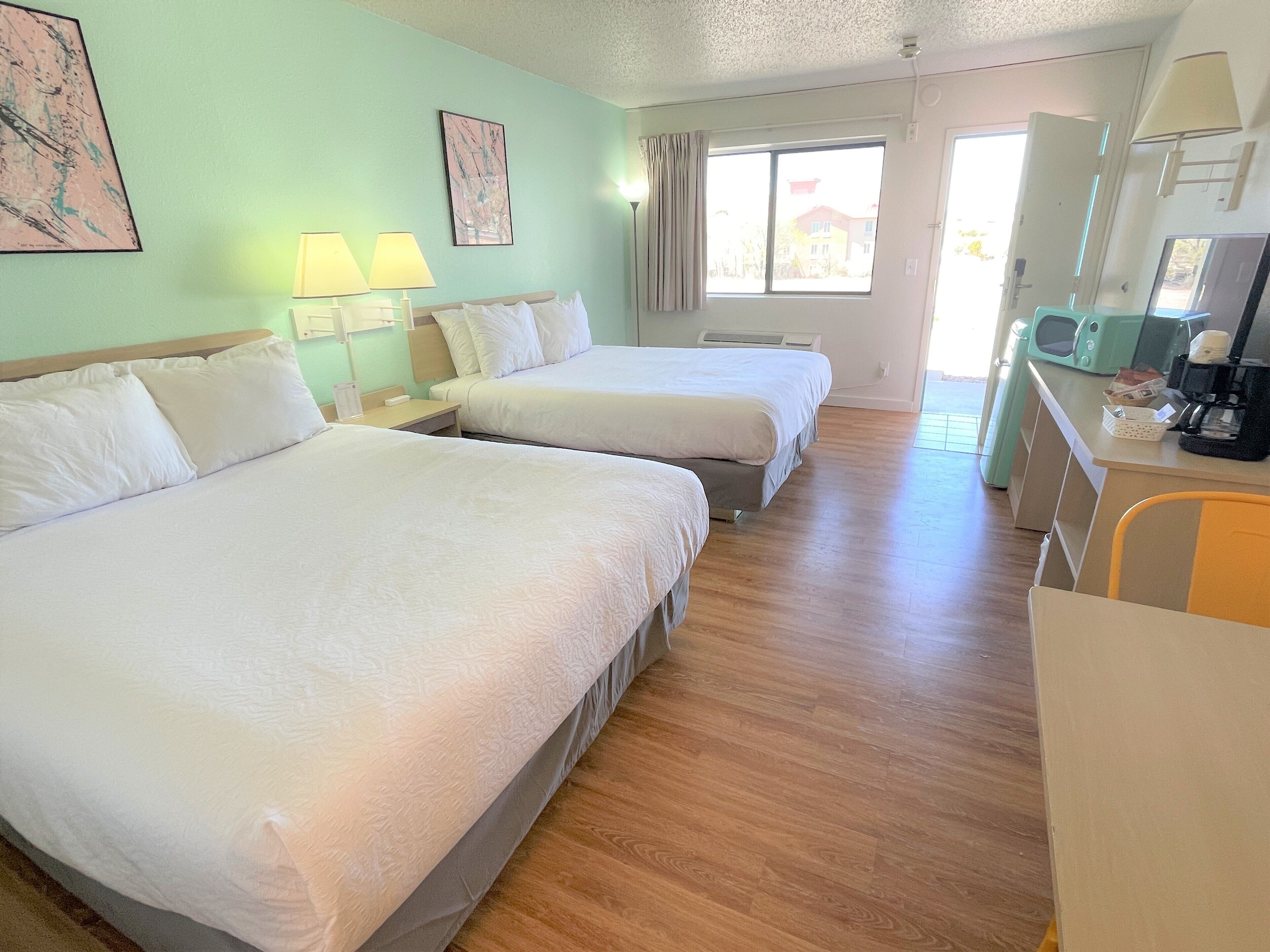 Habitación de hotel con dos camas, un escritorio, una silla, una ventana y una kitchenette.