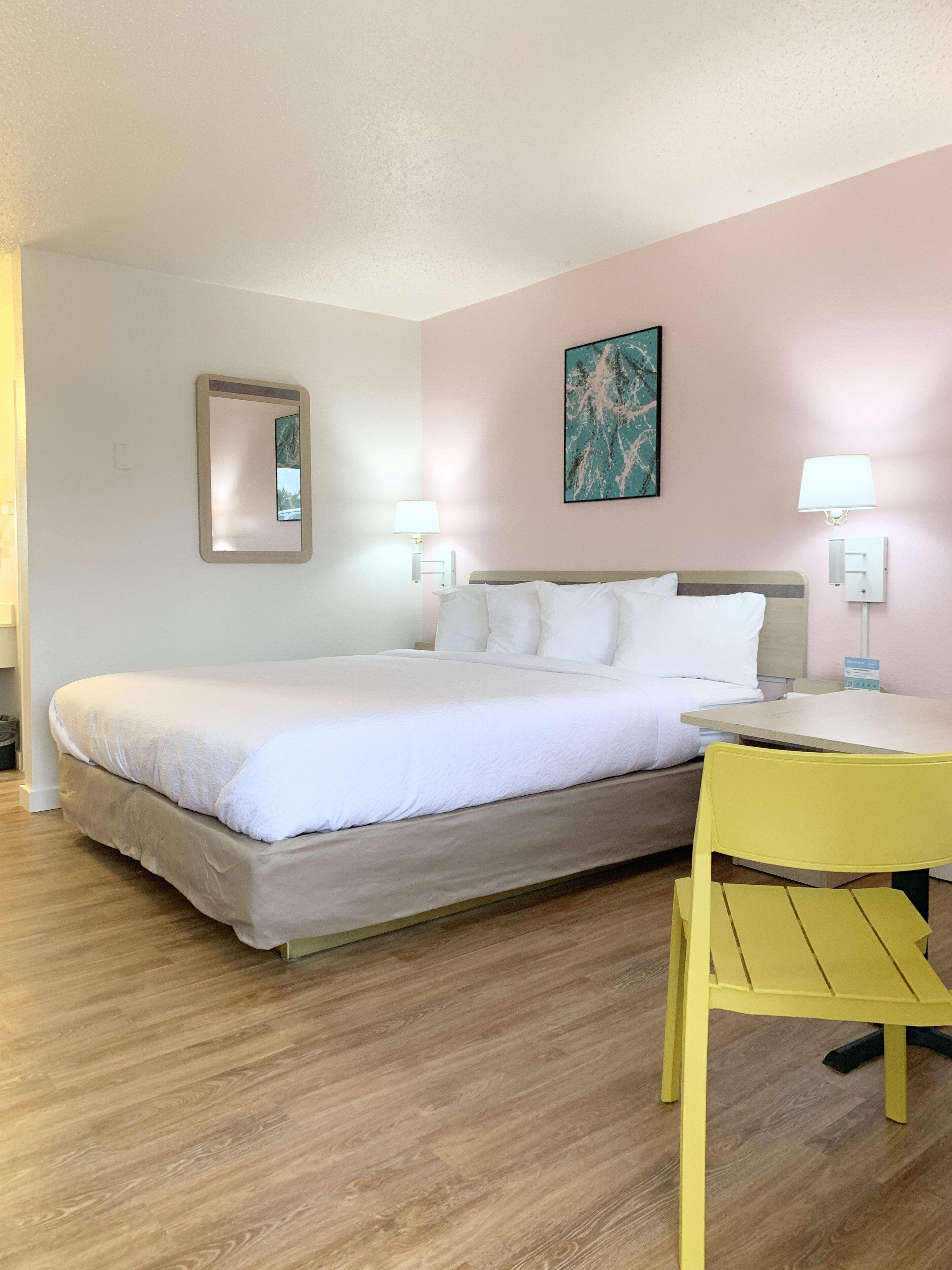Quarto de hotel bem arrumado, com cama, abajures, escrivaninha e uma cadeira.