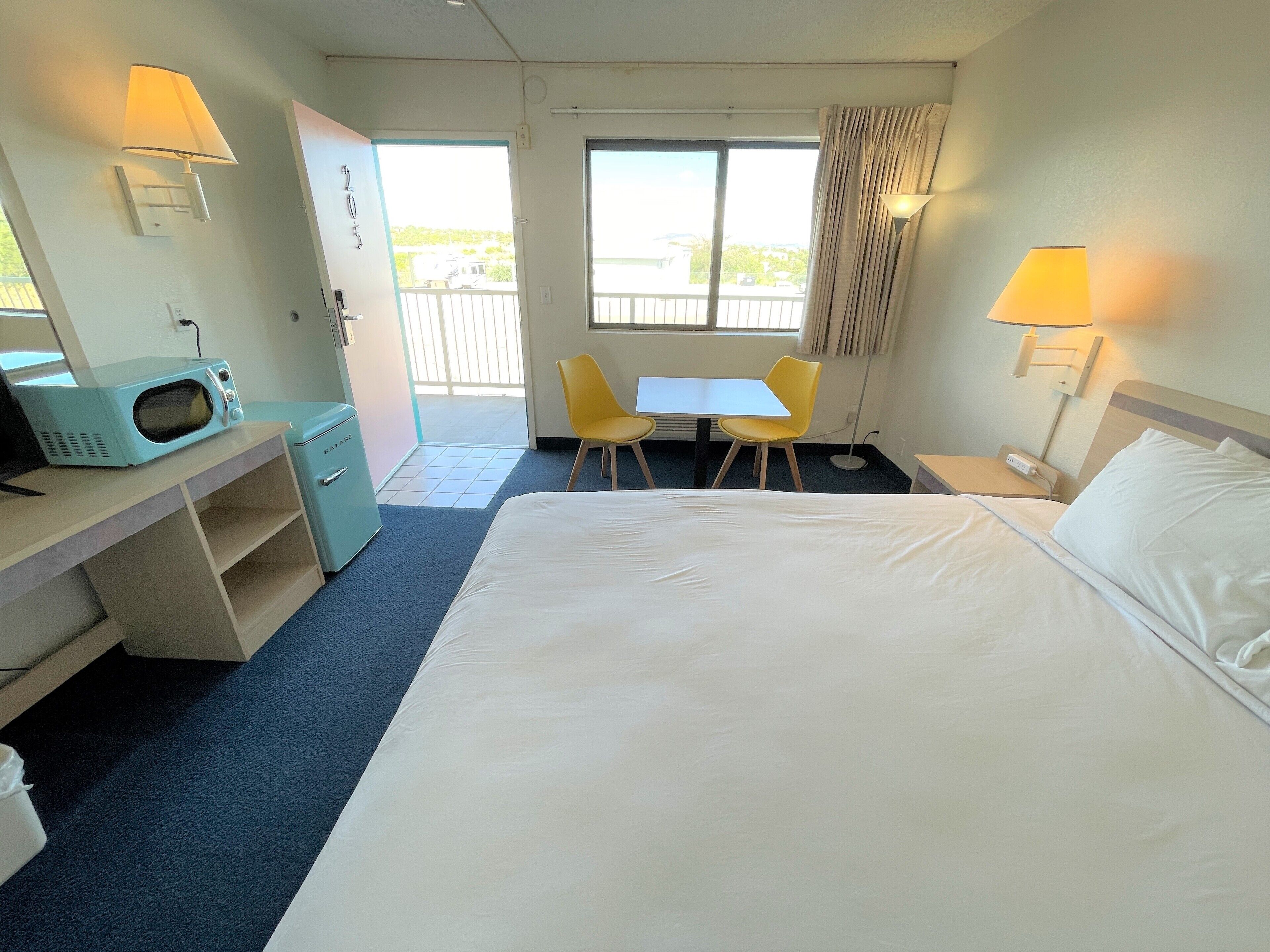 Een hotelkamer met een bed, een bureau met een magnetron, twee stoelen, een tafel en een raam met gordijnen.
