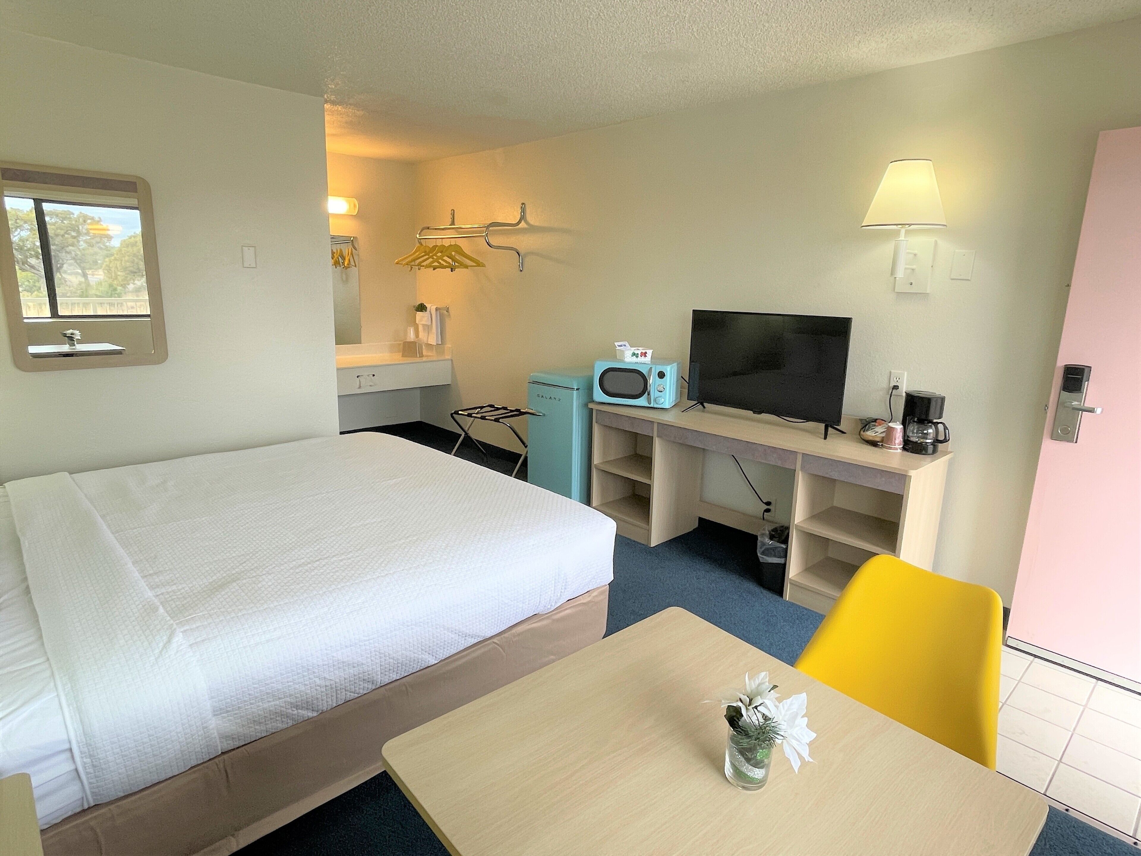Una habitación de hotel con cama, escritorio, televisión, microondas y cafetera.
