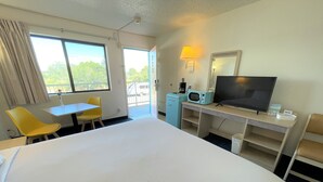 Habitación de hotel con una cama grande, un escritorio con ordenador, televisión y ventana con cortinas.