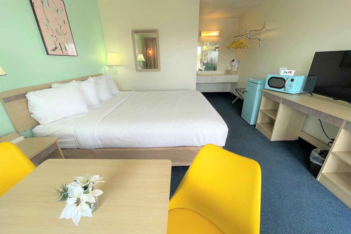 Una habitación de hotel con cama, escritorio, televisor, microondas y una silla.