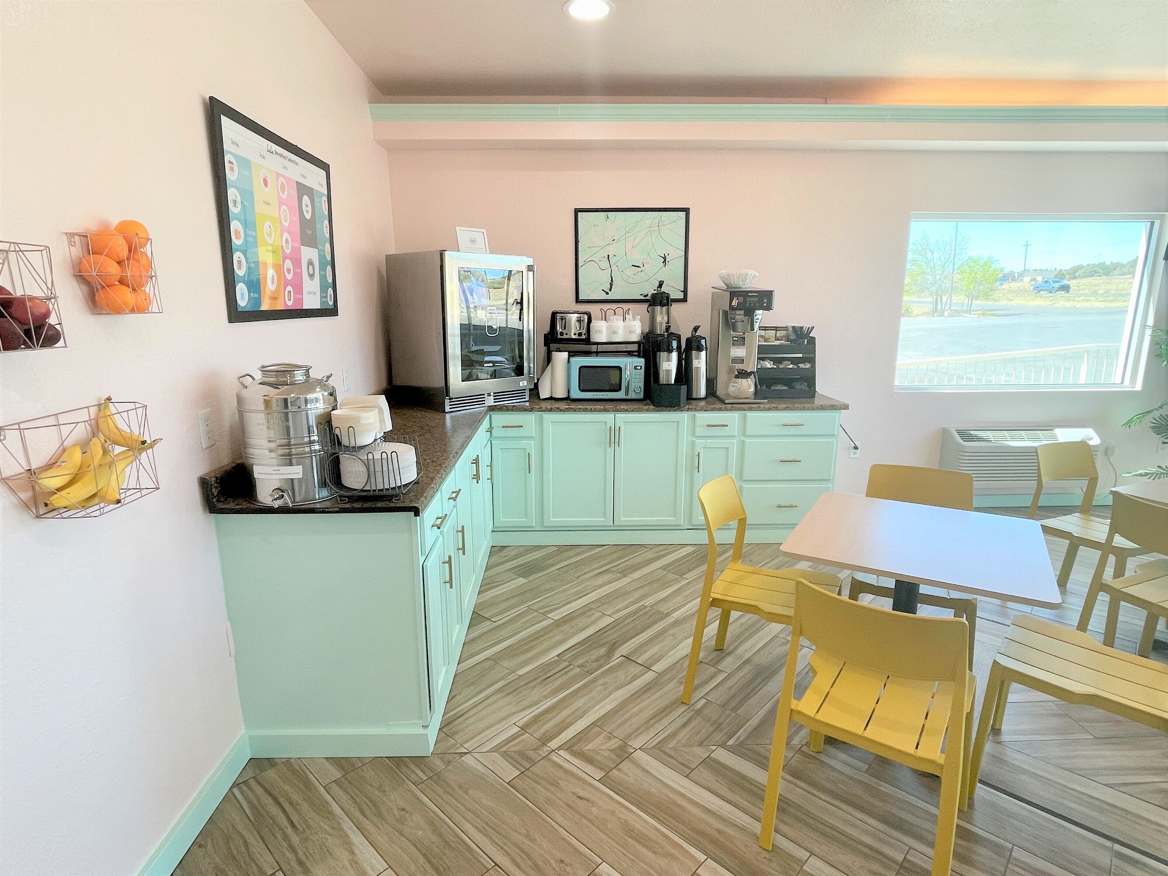 A kitchen with light green cabinets, a microwave, a coffee maker, and a dining area with yellow chairs and a white table.