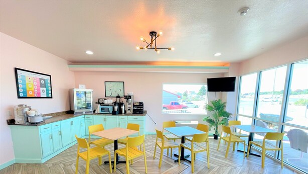 Una habitación luminosa con sillas amarillas y una mesa, una zona de cocina con microondas, y un ventanal con vistas al exterior.