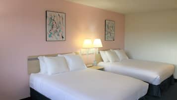 A hotel room with two single beds, a nightstand with a lamp, and two framed abstract paintings on the wall.
