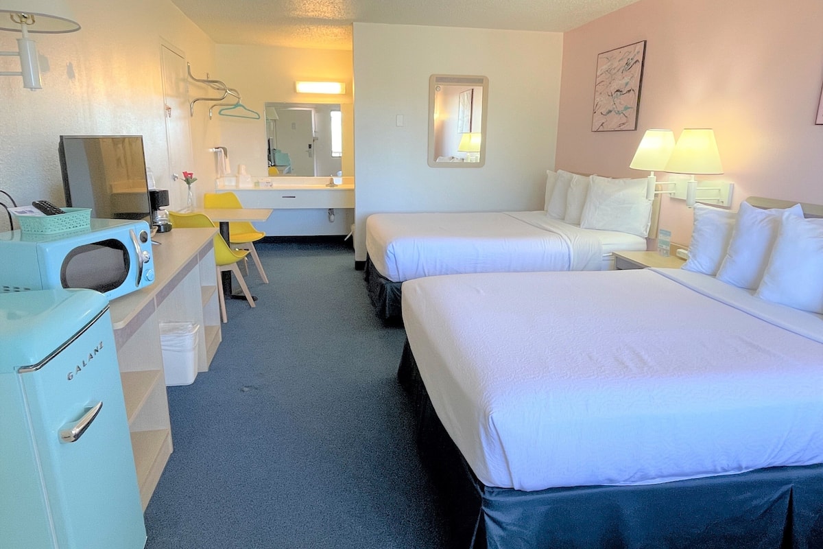 Una habitación de hotel con dos camas, un escritorio, una silla, un microondas, un lavabo y un espejo.