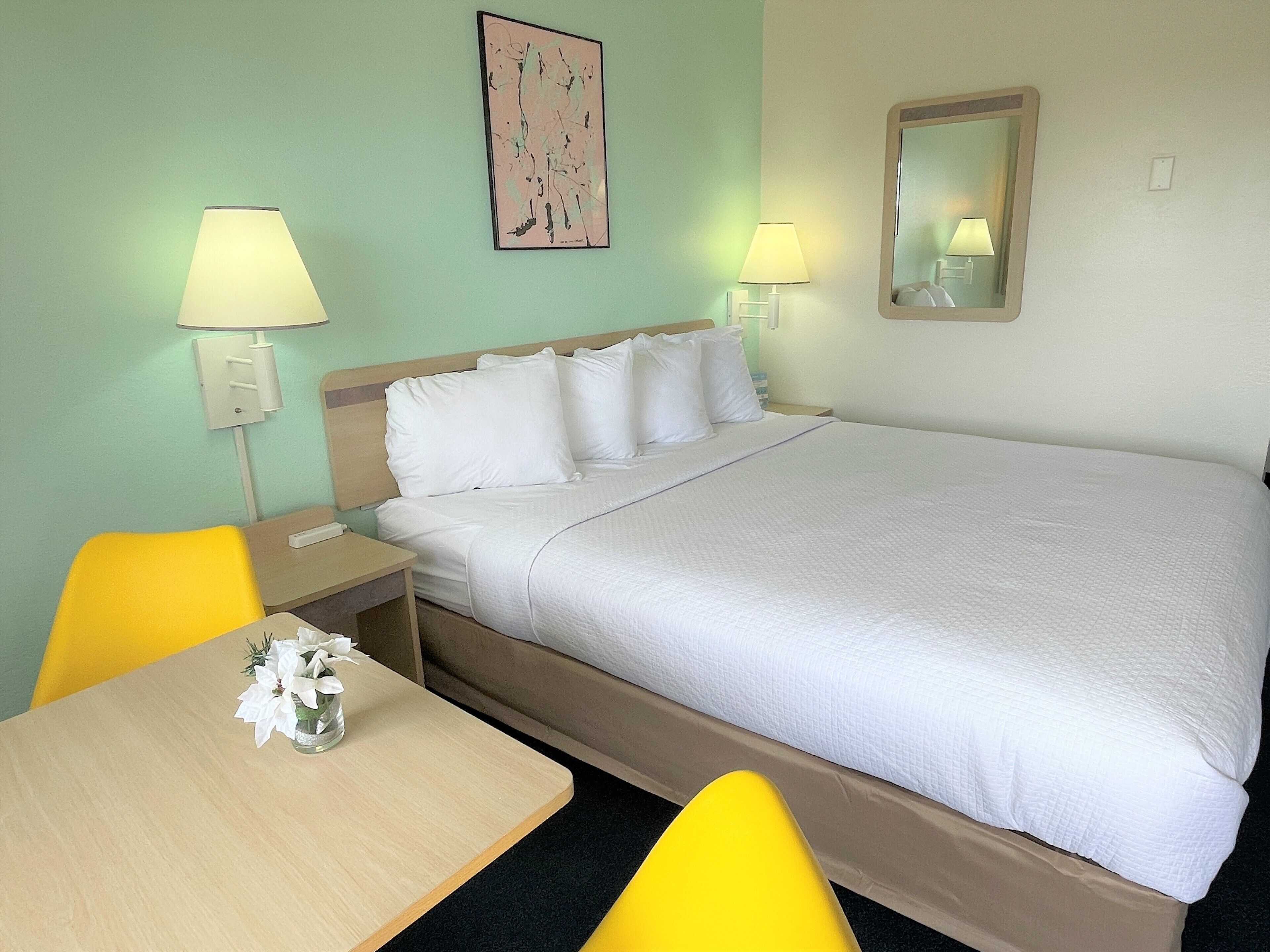 A hotel room with a bed, two bedside lamps, a bedside table with a vase of flowers, and a chair.