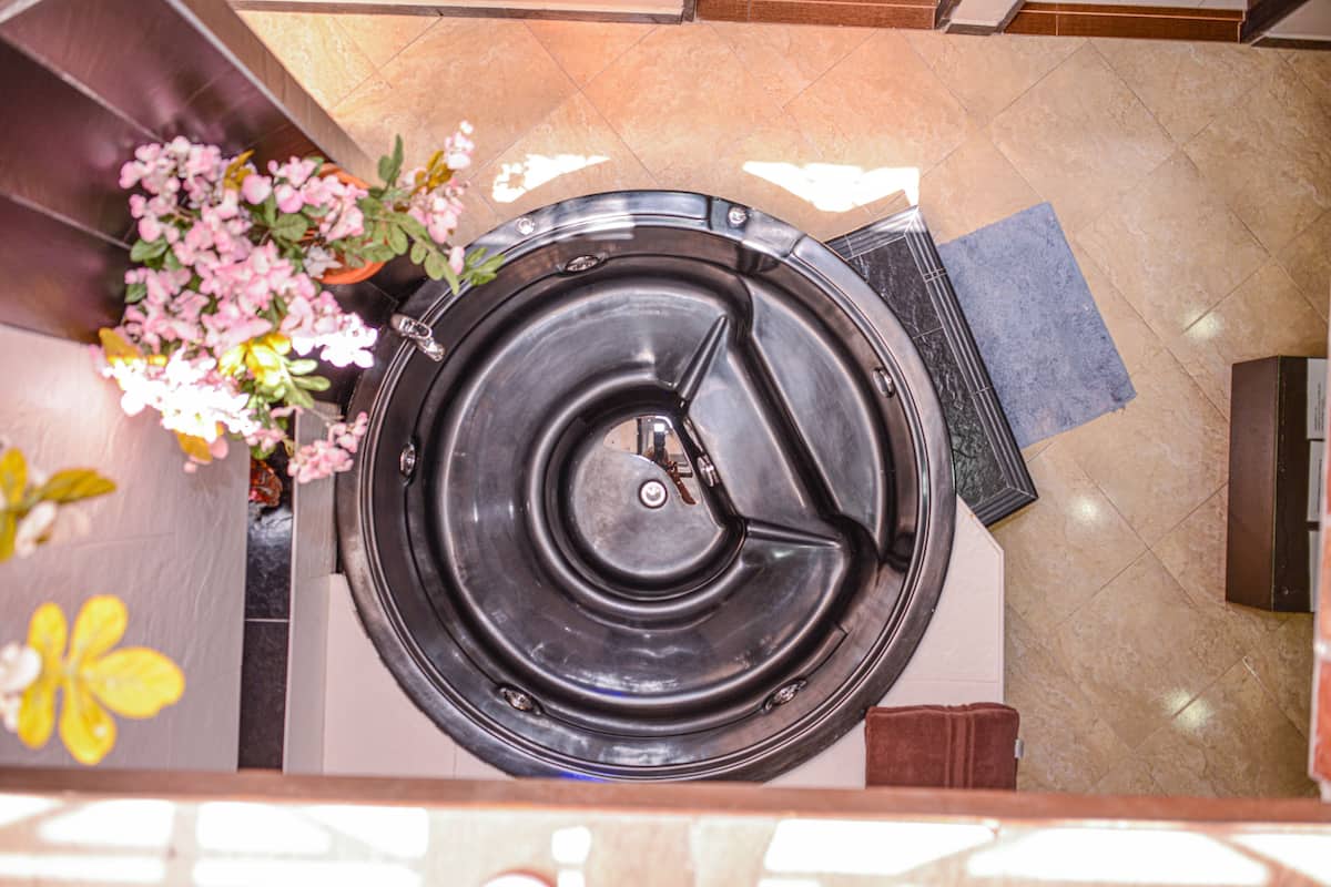A circular hot tub with a metallic finish, surrounded by a tiled floor with a beige pattern.