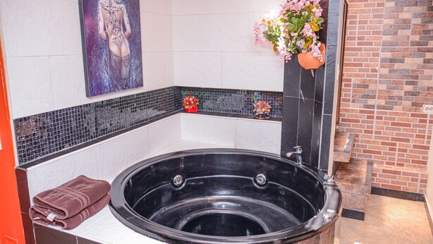 Ein Spa-Raum mit einer großen, schwarzen Badewanne, einem Handtuch, einer dekorativen Blumenanordnung und einem gerahmten Kunstwerk an der Wand.