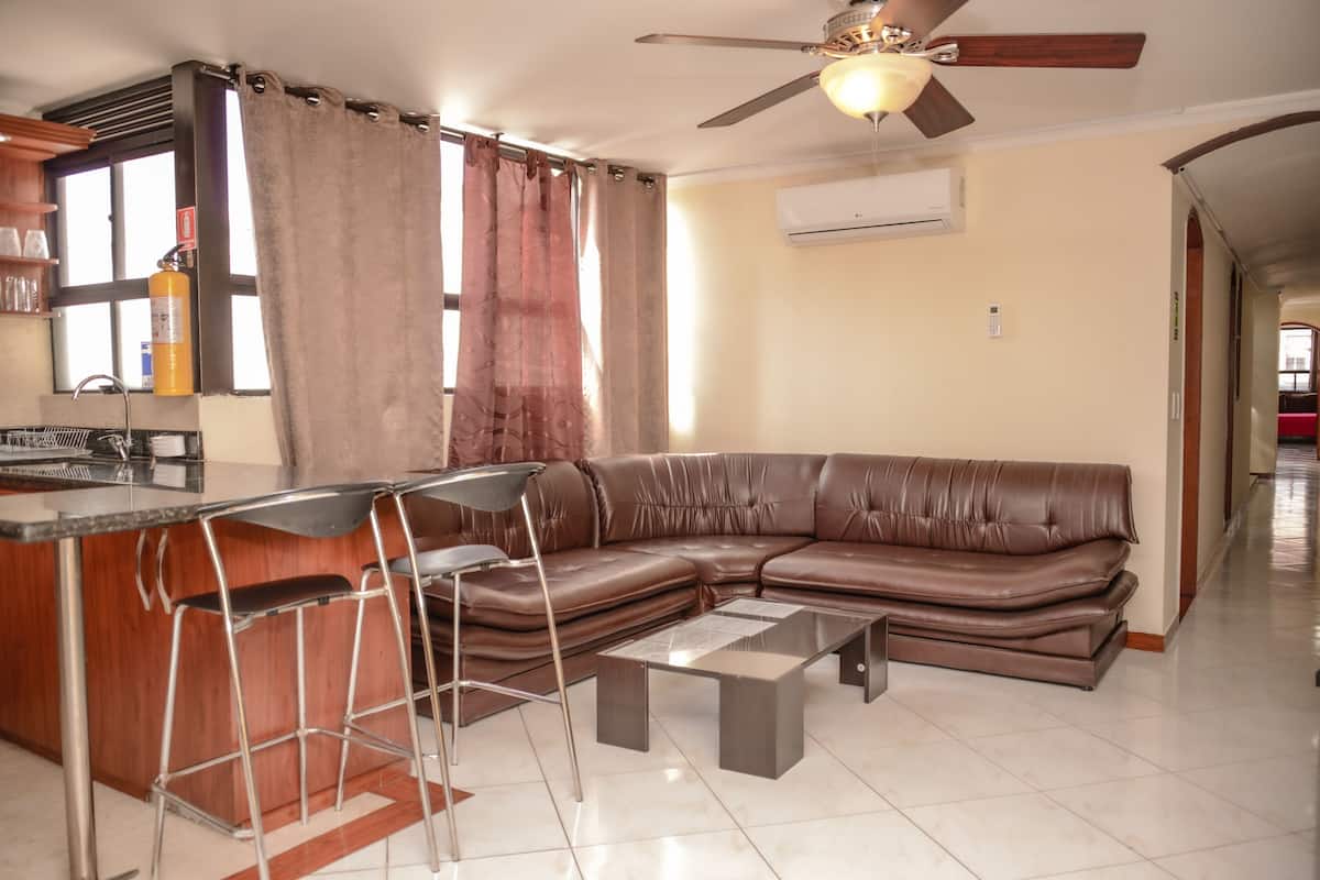 A living room with a brown leather sofa, a glass coffee table, and a bar area with stools.