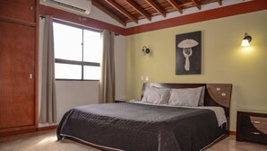 Ein Schlafzimmer mit Bett, Fenster mit Vorhängen, Wandlampe und einem Gemälde.