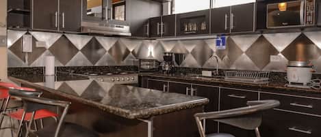 Una cocina moderna con armarios oscuros, encimera de granito y electrodomésticos de acero inoxidable. Hay dos taburetes de bar y un microondas en la encimera.