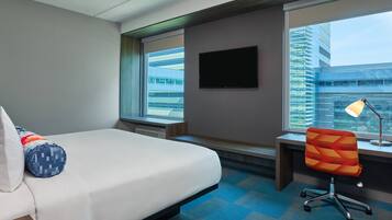 Una habitación de hotel con cama, escritorio, silla, televisión y ventana con vista a la ciudad.