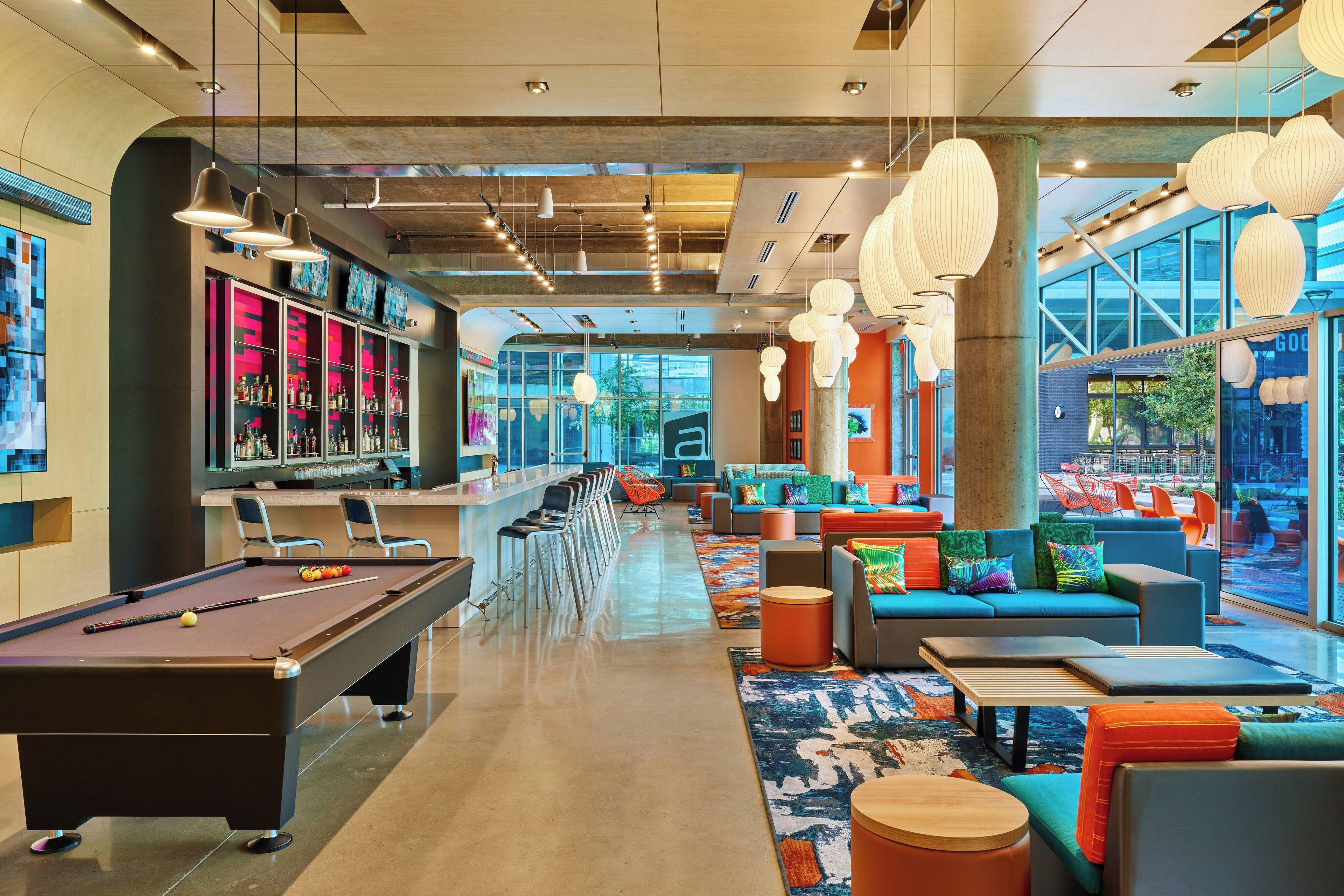A modern lounge area with a pool table, seating, and a bar.