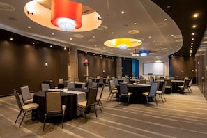 A conference room with round tables, chairs, and a large screen. - Aloft by Marriott Richardson (Plano)