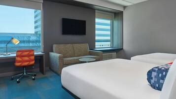 A hotel room with a bed, a desk with a chair, a television, and a window with a view of buildings.