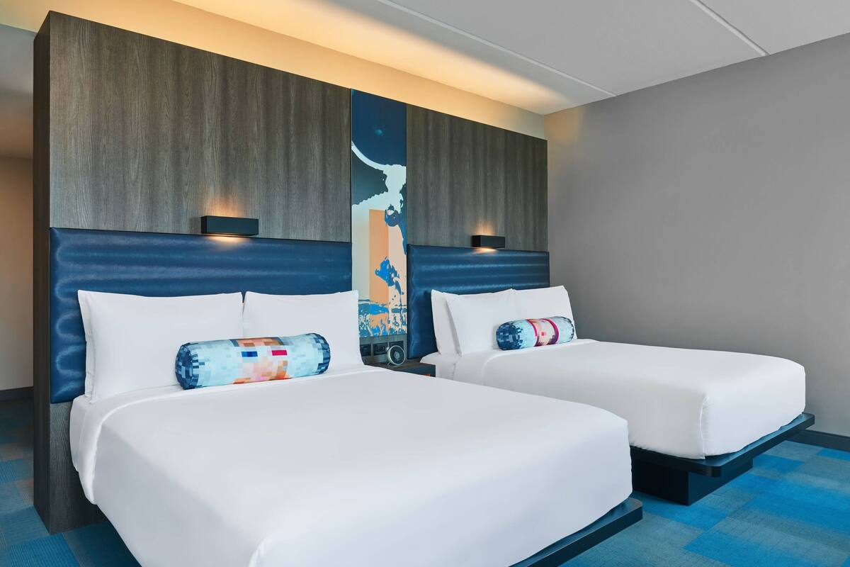 Quarto de hotel com duas camas, cada uma com cabeceira e travesseiro.