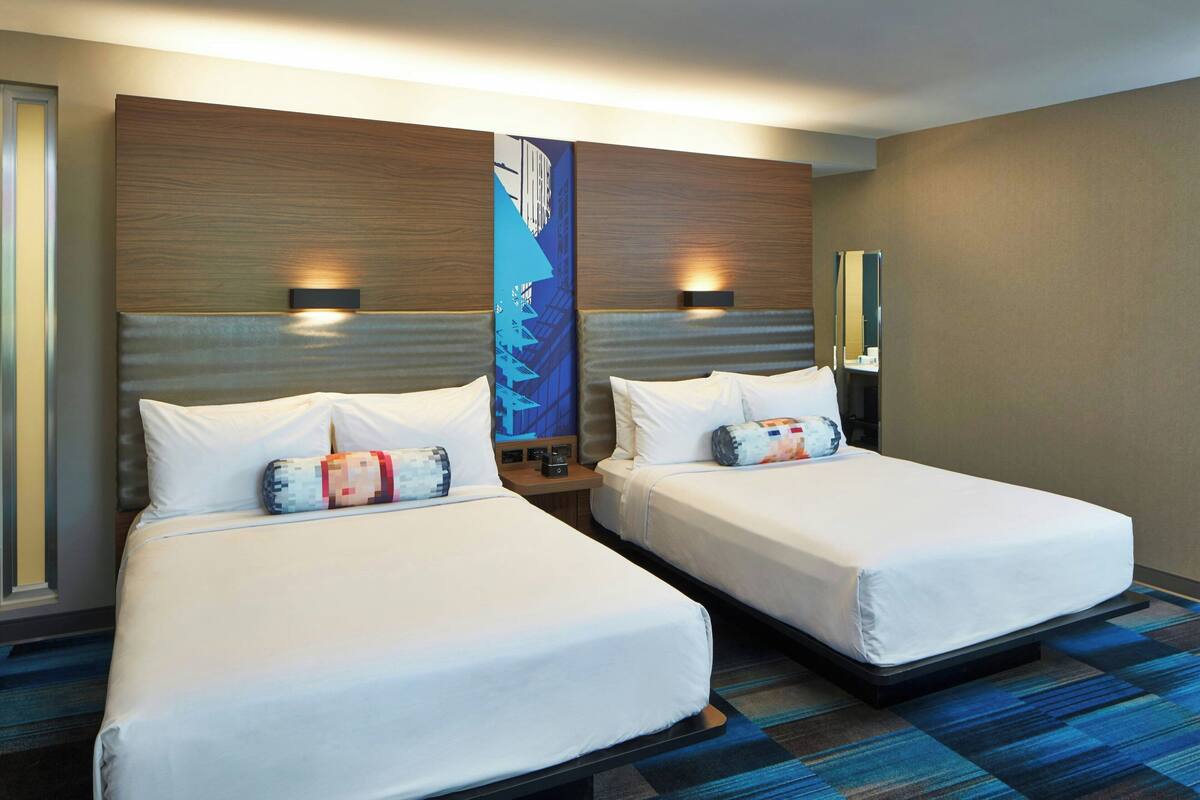 A hotel room with two beds, a large wall art piece, and a mirror.