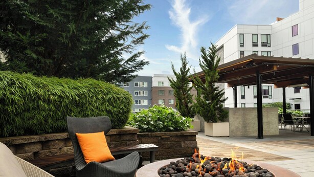 An outdoor patio area with a fire pit, seating, and a view of buildings in the background.