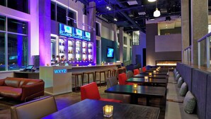 A modern bar area with a neon sign, seating arrangements, and a television screen.