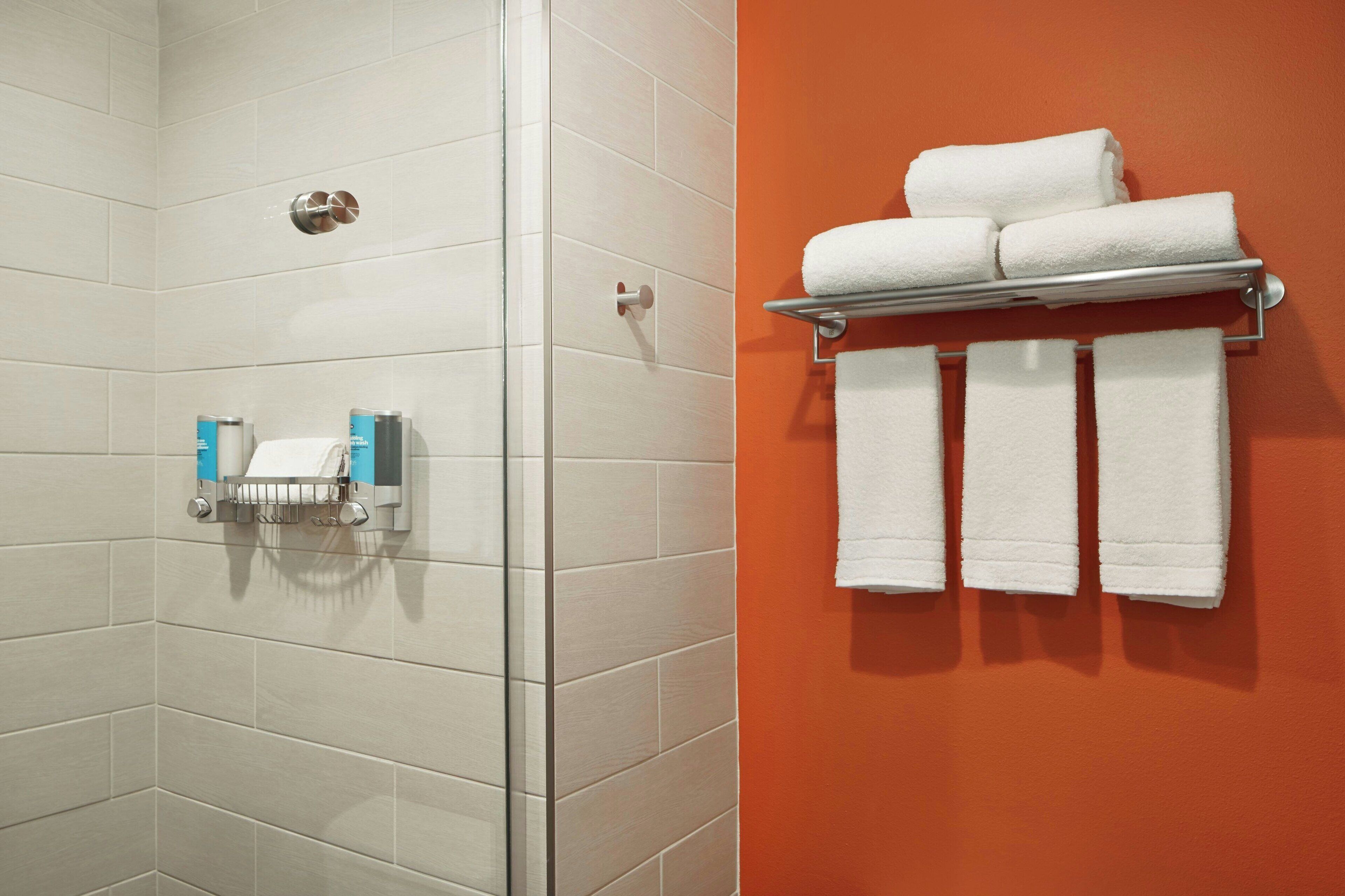 Een badkamer met witte tegels, een douche en een handdoekrek met witte handdoeken.