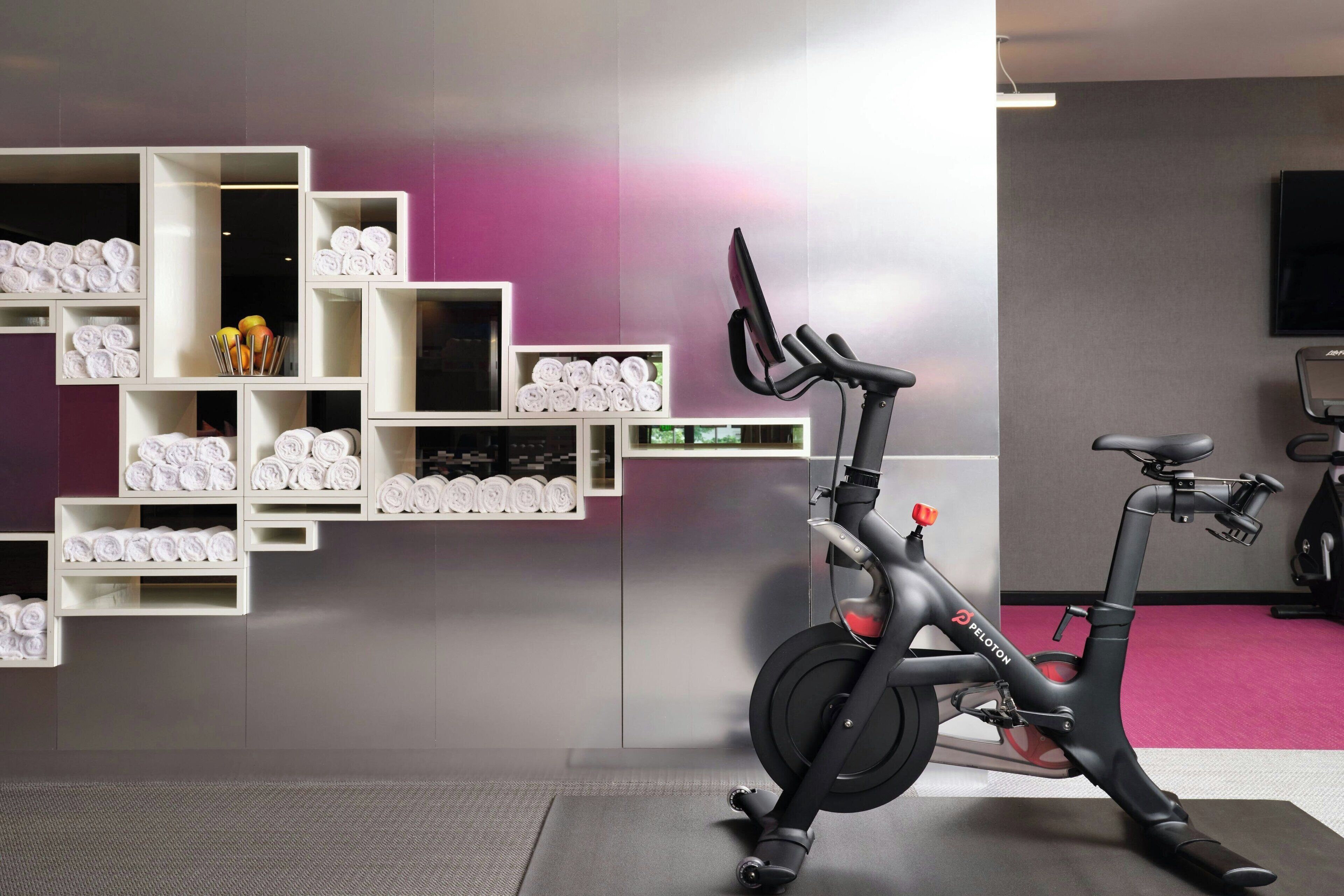 A stationary bike in a room with a purple wall and shelves of rolled towels.