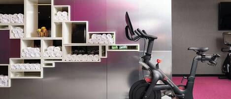 A stationary bike in a room with a purple wall and shelves of rolled towels.