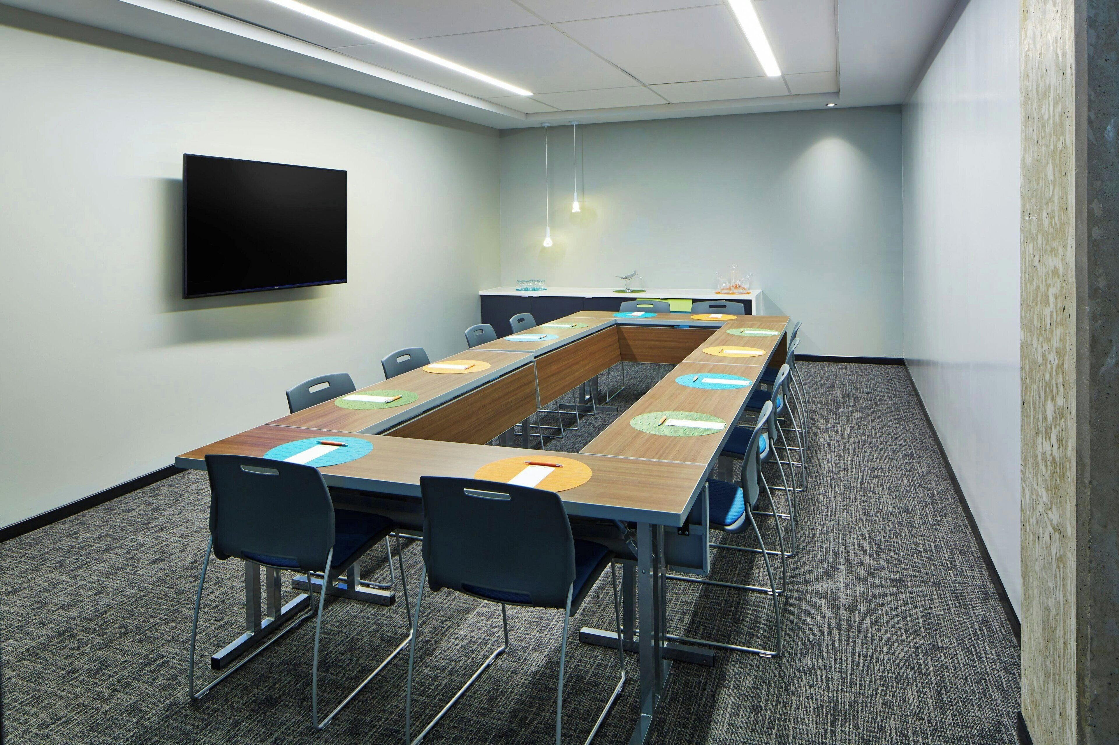 A conference room with a long table, chairs, a flat-screen TV, and a carpeted floor.