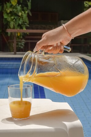 Eine Hand gießt Orangensaft aus einem Glasgefäß in ein Glas.