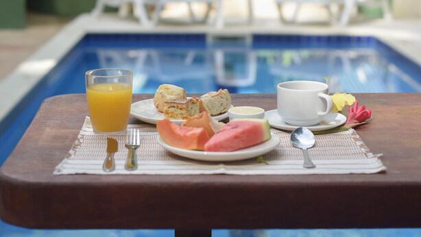 Desayuno junto a una piscina con una bebida, tostadas y fruta.