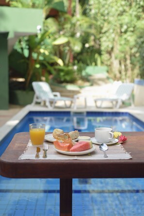 Desayuno junto a una piscina con una bebida, tostadas y fruta.