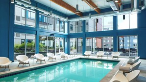 A modern indoor pool area with clear glass walls, multiple seating areas, and a view of the outside buildings. - Element by Marriott Seattle Redmond (Redmond)