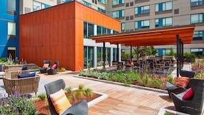 An outdoor patio area with wicker furniture, a wooden pergola, and a view of a modern building with multiple windows. - Element by Marriott Seattle Redmond (Redmond)