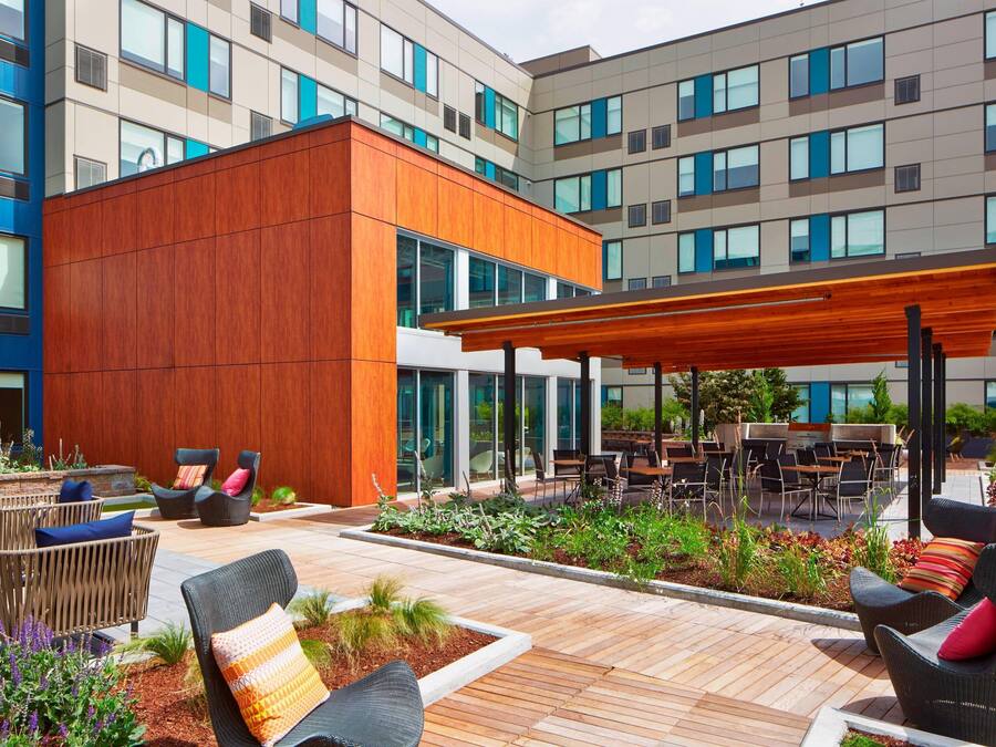 Un espace extérieur aménagé en terrasse, avec des meubles en osier, une pergola en bois et une vue sur un bâtiment moderne doté de nombreuses fenêtres.