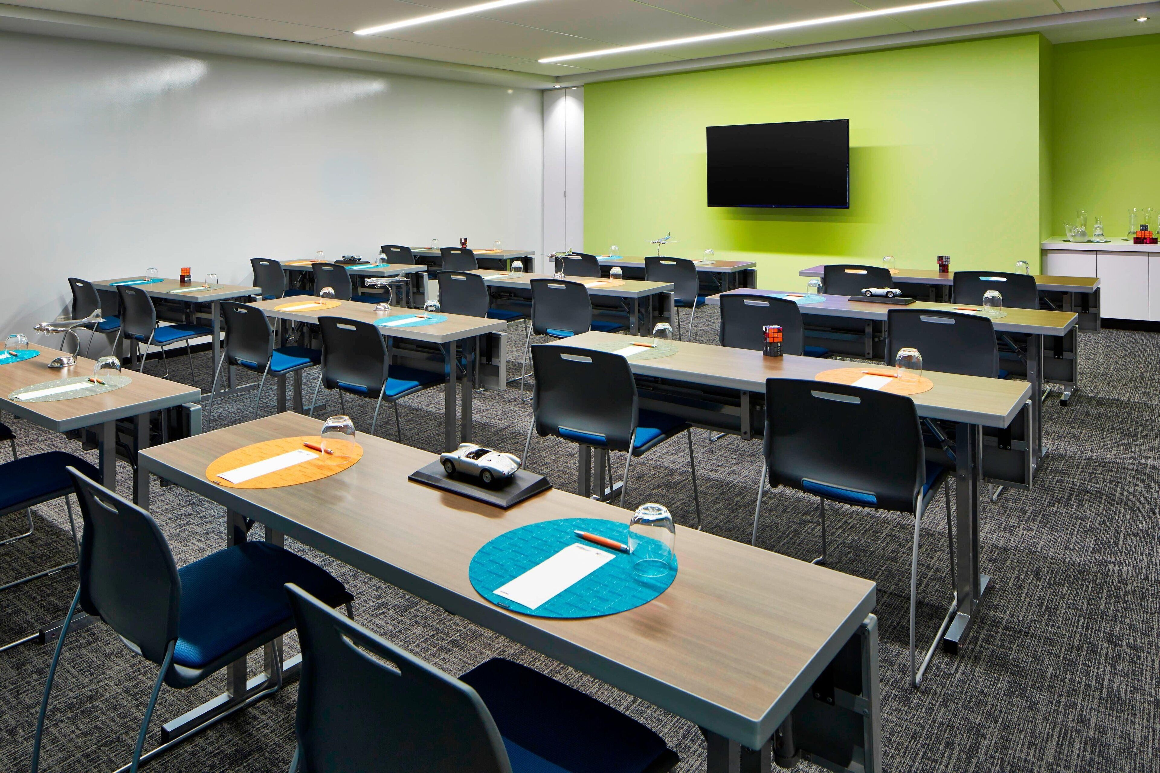 A classroom with rows of tables and chairs, a projector screen, and a green accent wall.
