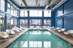 A swimming pool with lounge chairs and large windows.