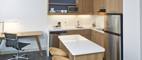 Una cocina moderna con armarios de madera, un refrigerador de acero inoxidable, un microondas y un lavavajillas. Hay una mesa de comedor de madera con dos sillas y un taburete de bar.