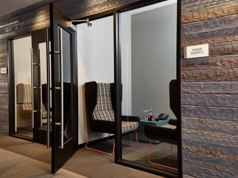 A modern conference room with glass walls, a black-framed chair, a patterned chair, and a sign indicating 'Phone Booth 2'.