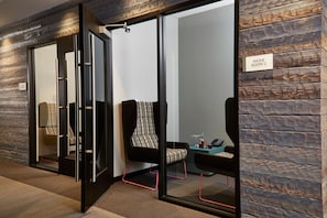 A modern conference room with glass walls, a black-framed chair, a patterned chair, and a sign indicating 'Phone Booth 2'.