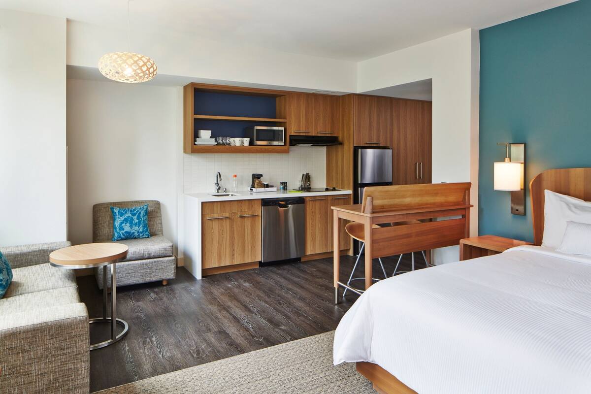 Una habitación de hotel moderna con kitchenette, una cama, un espacio de descanso con una pequeña mesa y un sofá.