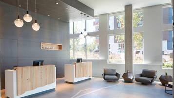A modern reception area with a wooden reception desk, two seating areas with contemporary chairs, and large windows allowing natural light.